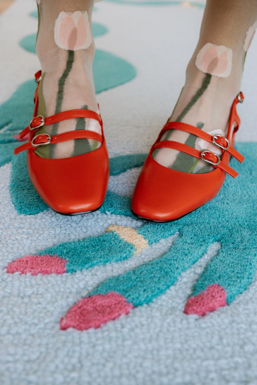 Red shoes standing on a large blue rug with a green wavy border and subtle gold silk accents