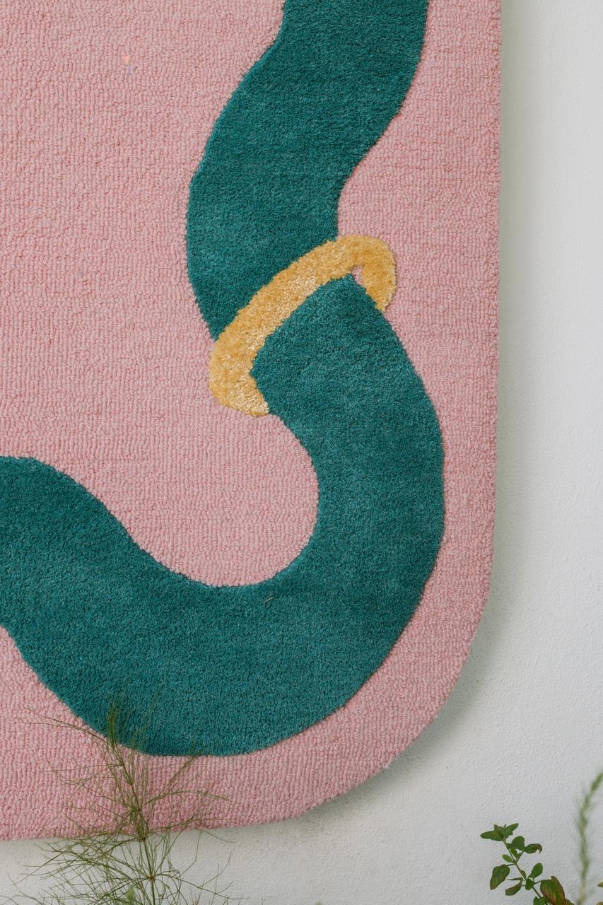 Large pink rug with green wavy arms along the border, accessorized with gold artificial silk accent jewellery