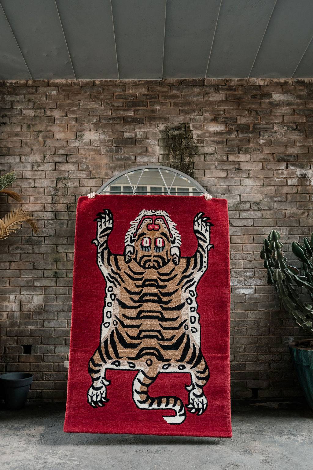 Maroon wool rug with a tiger design against a brick wall.