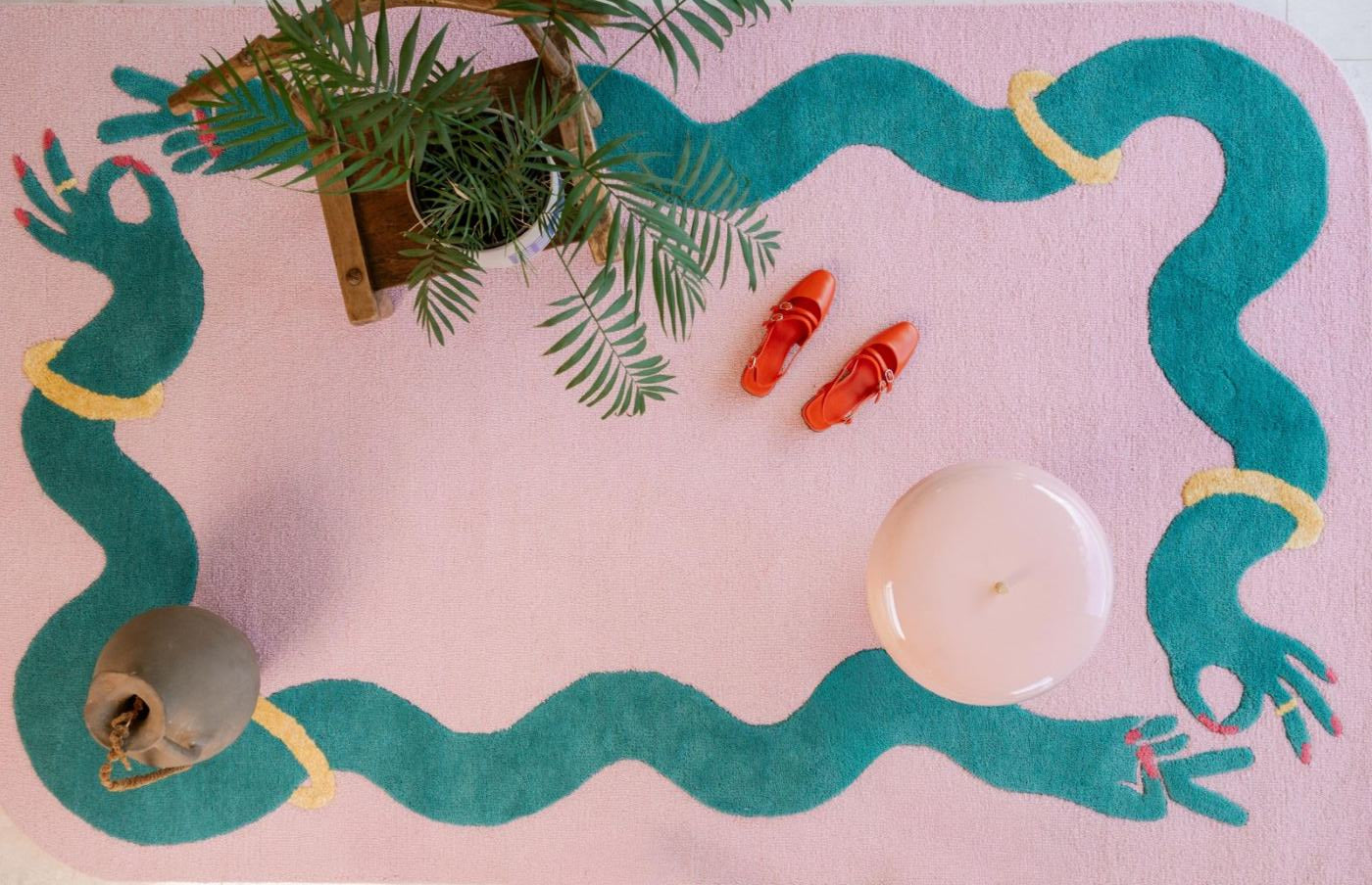 Large pink statement rug with a pair of red ladies shoes, a lamp and a plant on top