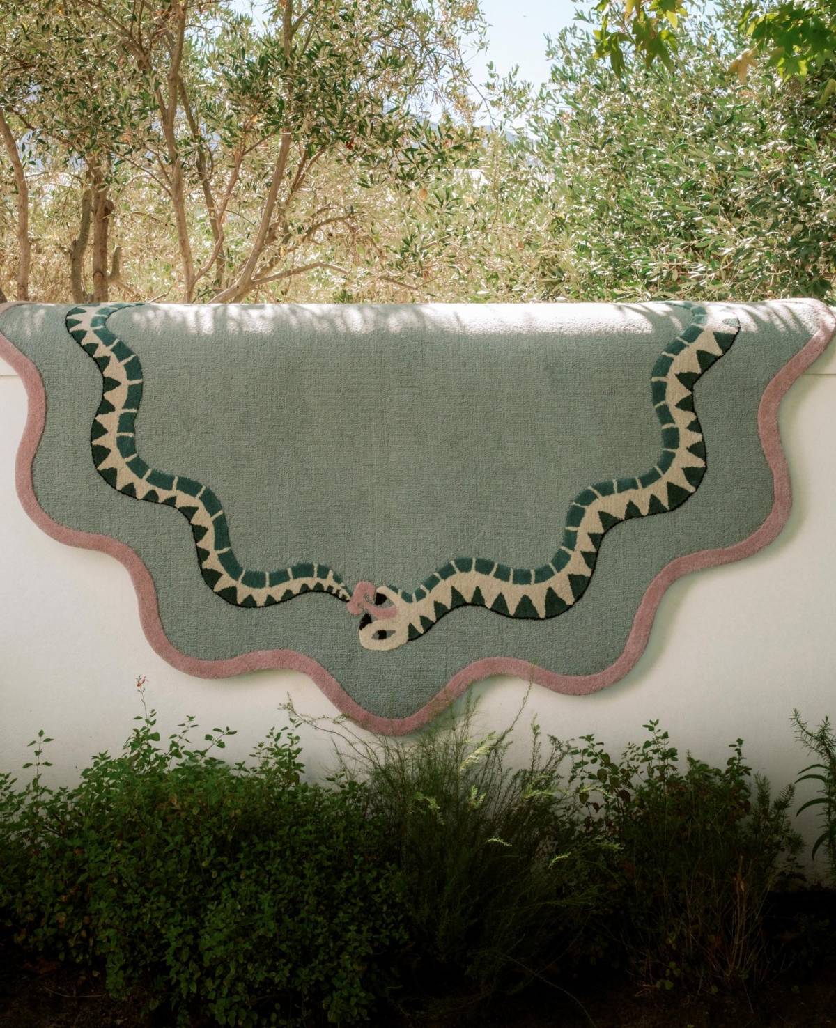 Decorative green rug with snake design on a white wall outdoors