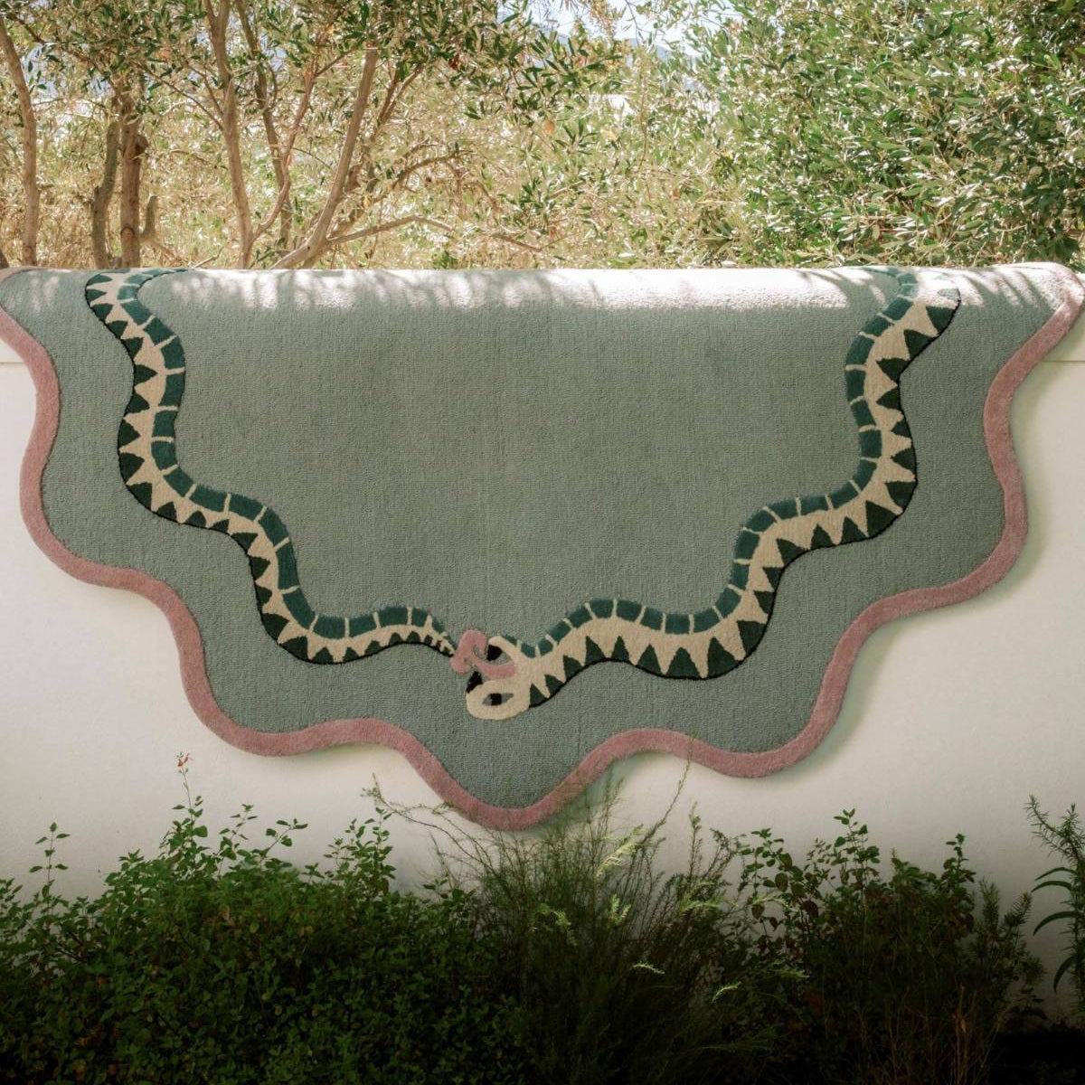 Decorative green rug with snake design on a white wall outdoors