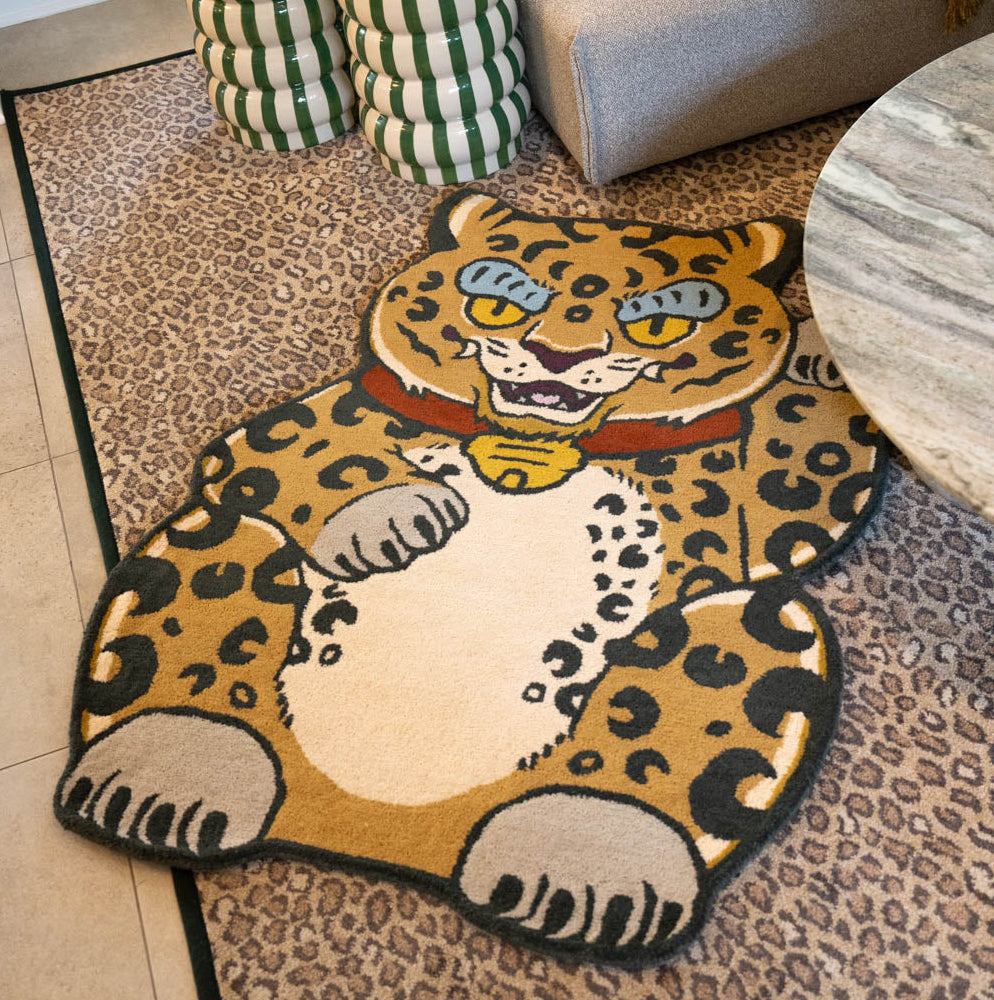 A leopard-shaped area rug featuring a japanese maneki neko-style leopard with a gold collar, displayed on a patterned area rug in a living room setting.