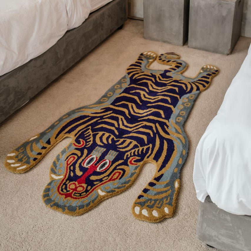 Decorative wool tibetan tiger rug on a carpeted floor in a bedroom setting with a bed and nightstands, south africa