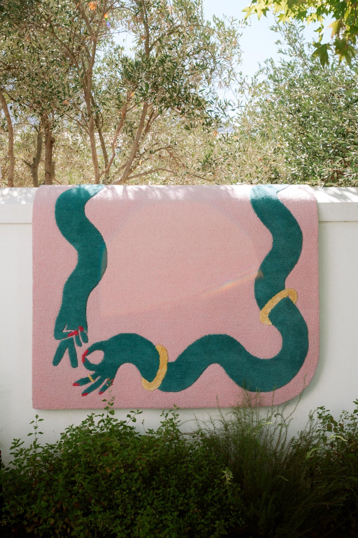 Pink wool rug with green and gold design hanging on a white wall outdoors.