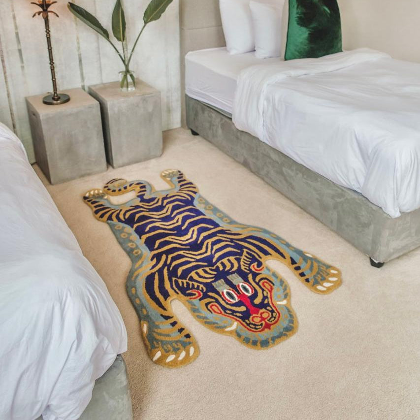 Decorative hand-tufted wool tibetan tiger statement rug on a bedroom floor with a bed and nightstands in the background. south africa