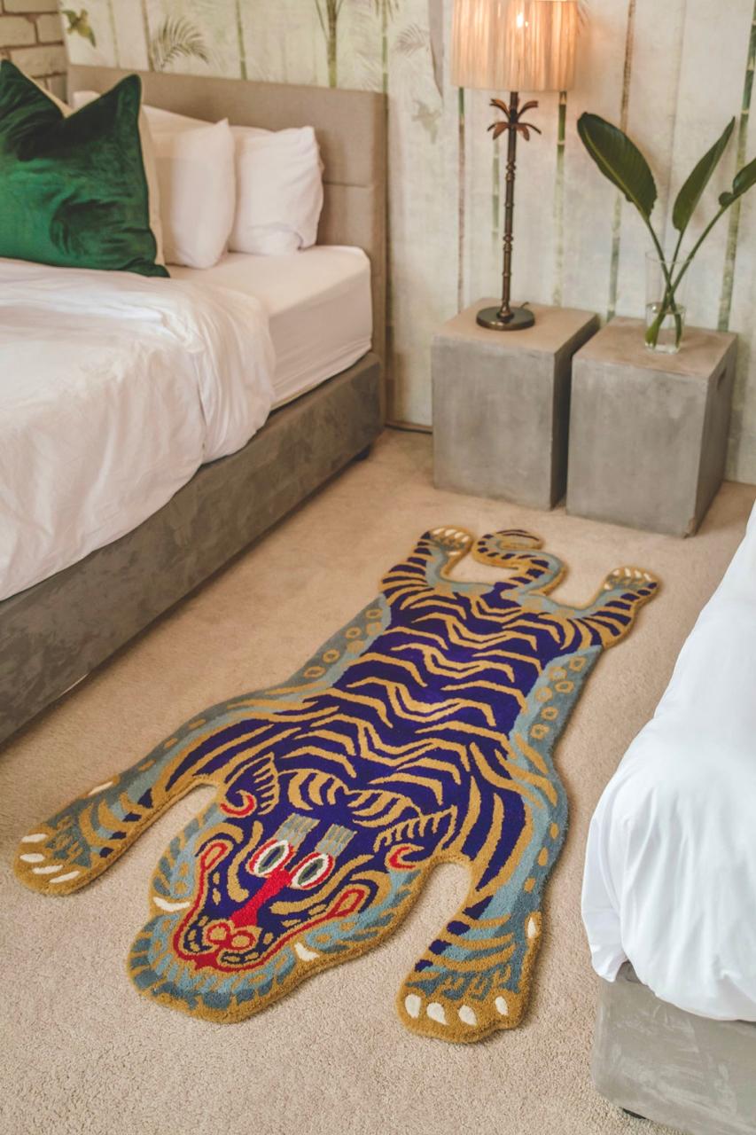 Hand-tufted wool tibetan tiger statement rug on a beige carpet in a bedroom setting with a bed and nightstands.